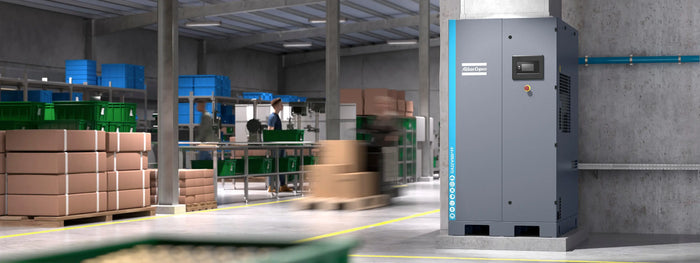Image showing an industrial air compressor positioned in a warehouse where staff appear blurred as they work around the compressor