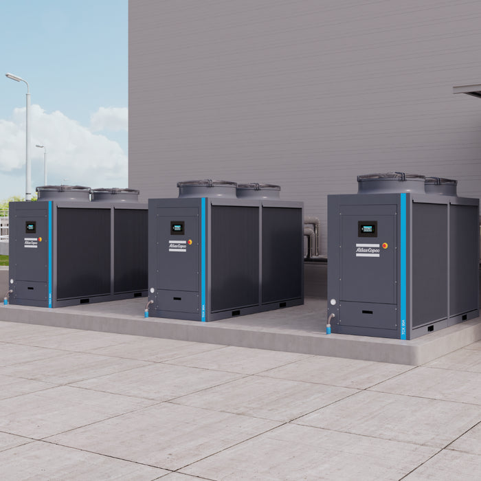 Three Atlas Copco TCX industrial chillers in an external setting sat on a concrete base with a grey wall behind them